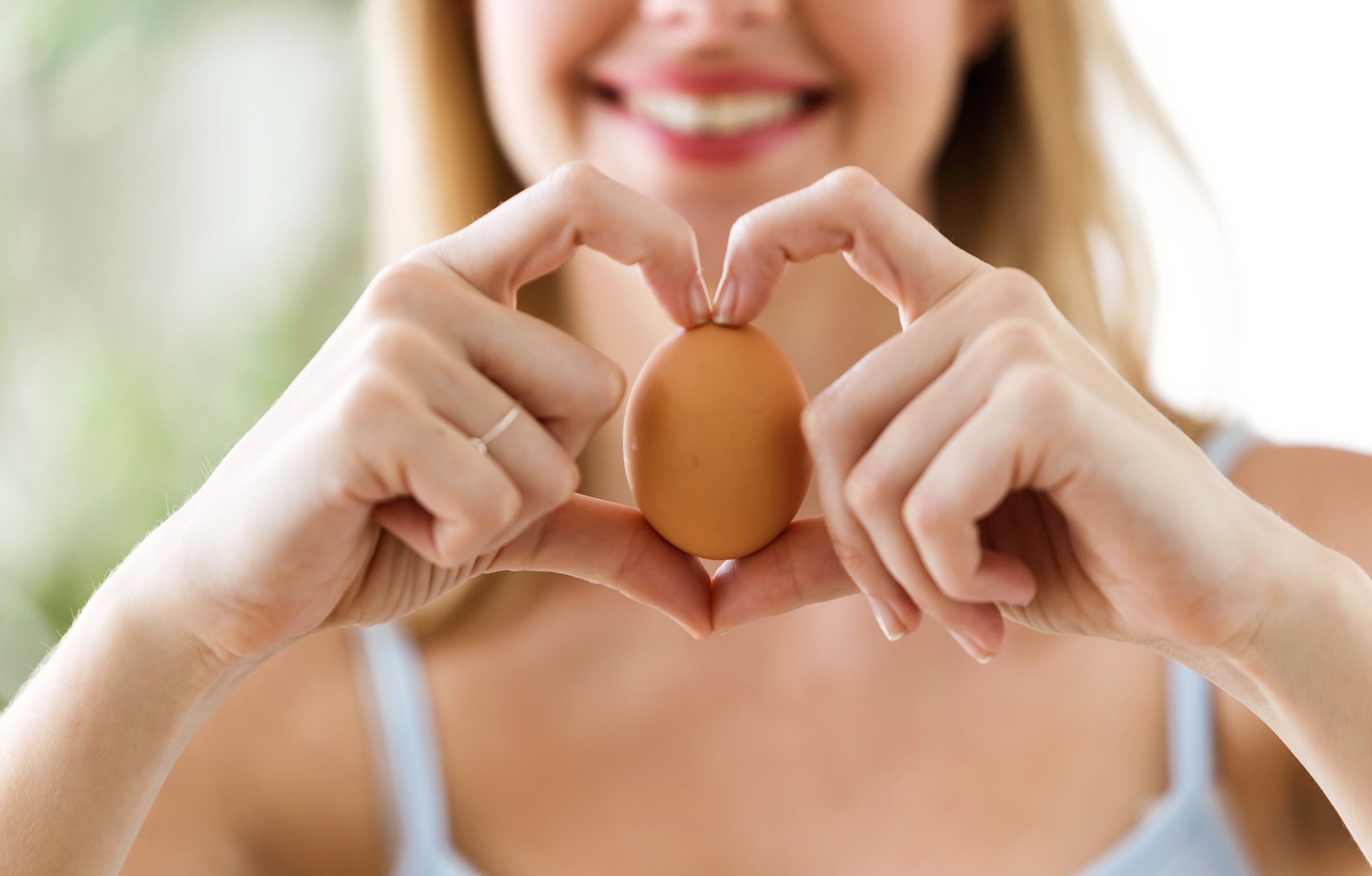 imagen de mujer joven sujetando un huevo y formando un corazón con los dedos